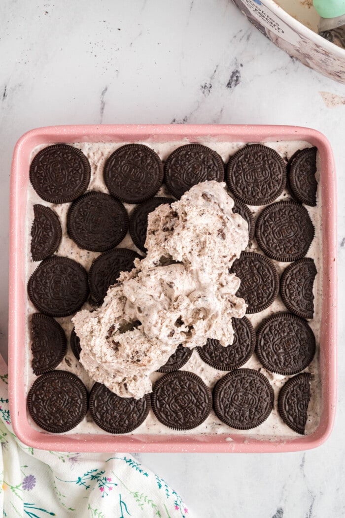 Cookies and cream ice cream being spread over a layer of Oreos