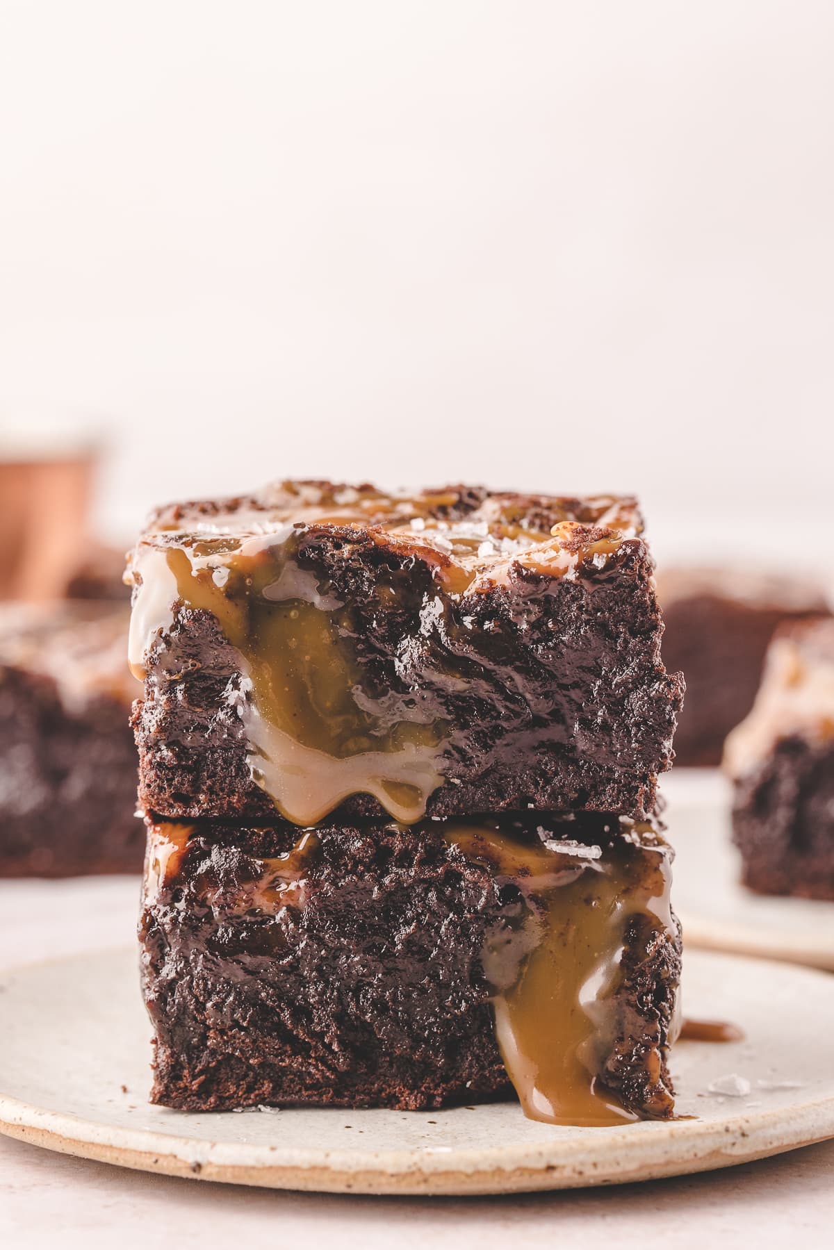 caramel brownies stacked on plate with more brownies in background