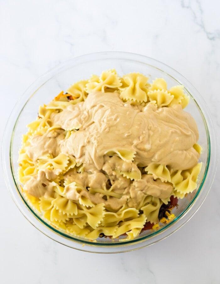 pasta in glass bowl with ingredients for cowboy pasta salad and dressing on top