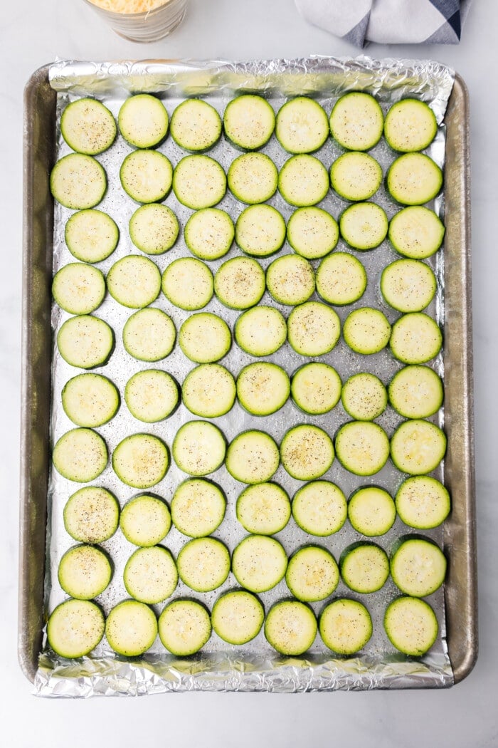 sliced zucchini on baking sheet with salt and pepper