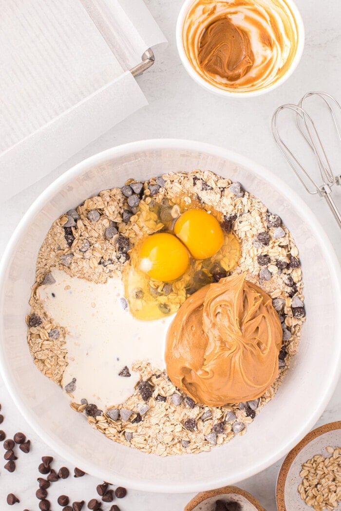 eggs, peanut butter and heavy cream in white bowl with oatmeal chocolate chip cookie mix