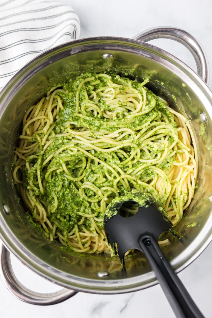 Pesto being mixed into spaghetti noodles