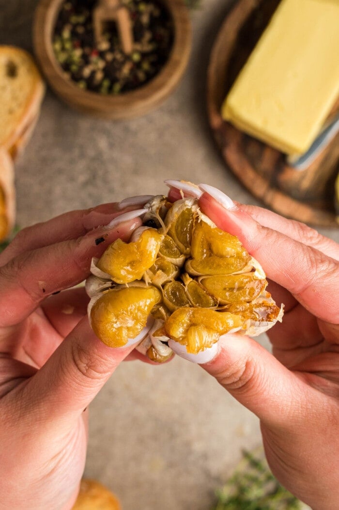 A hand squeezing roasted garlic from the bulb