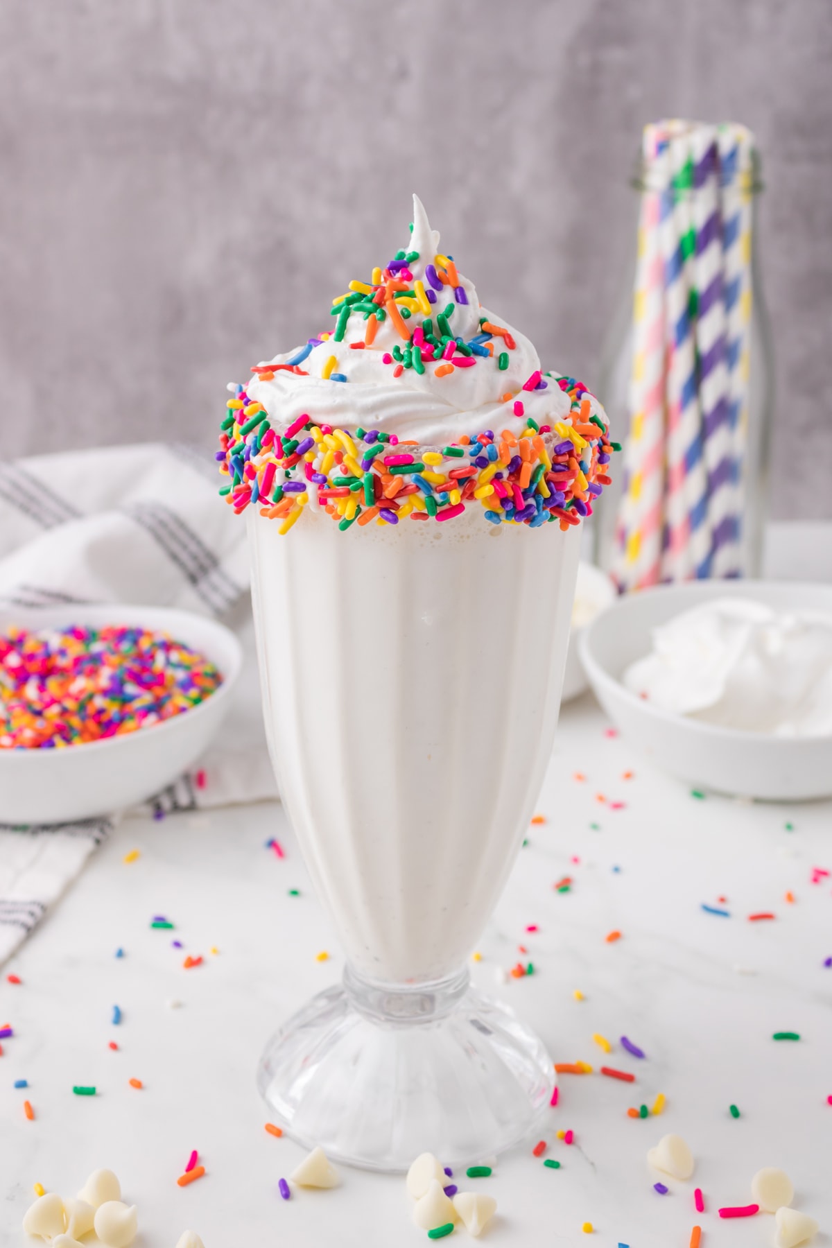 vanilla milkshake in tall glass with whip cream and rainbow sprinkles