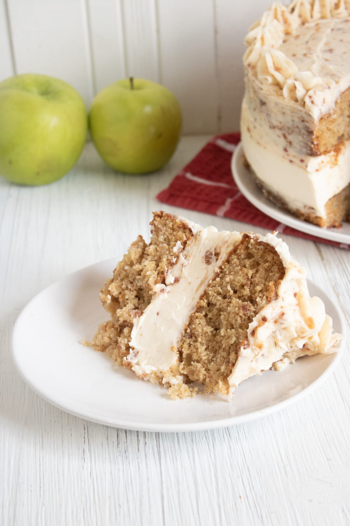 Apple Maple Bacon Cake with Cheesecake Filling with fresh apples in the back.