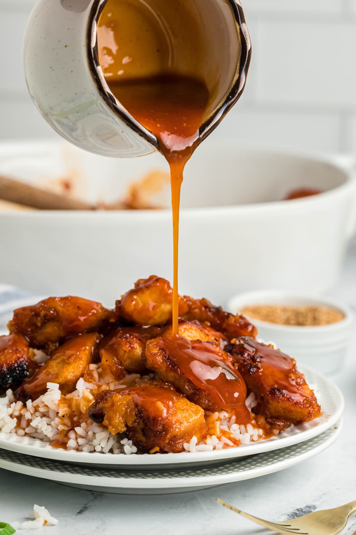 Sweet and sour sauce being drizzled over a plate of chicken and rice