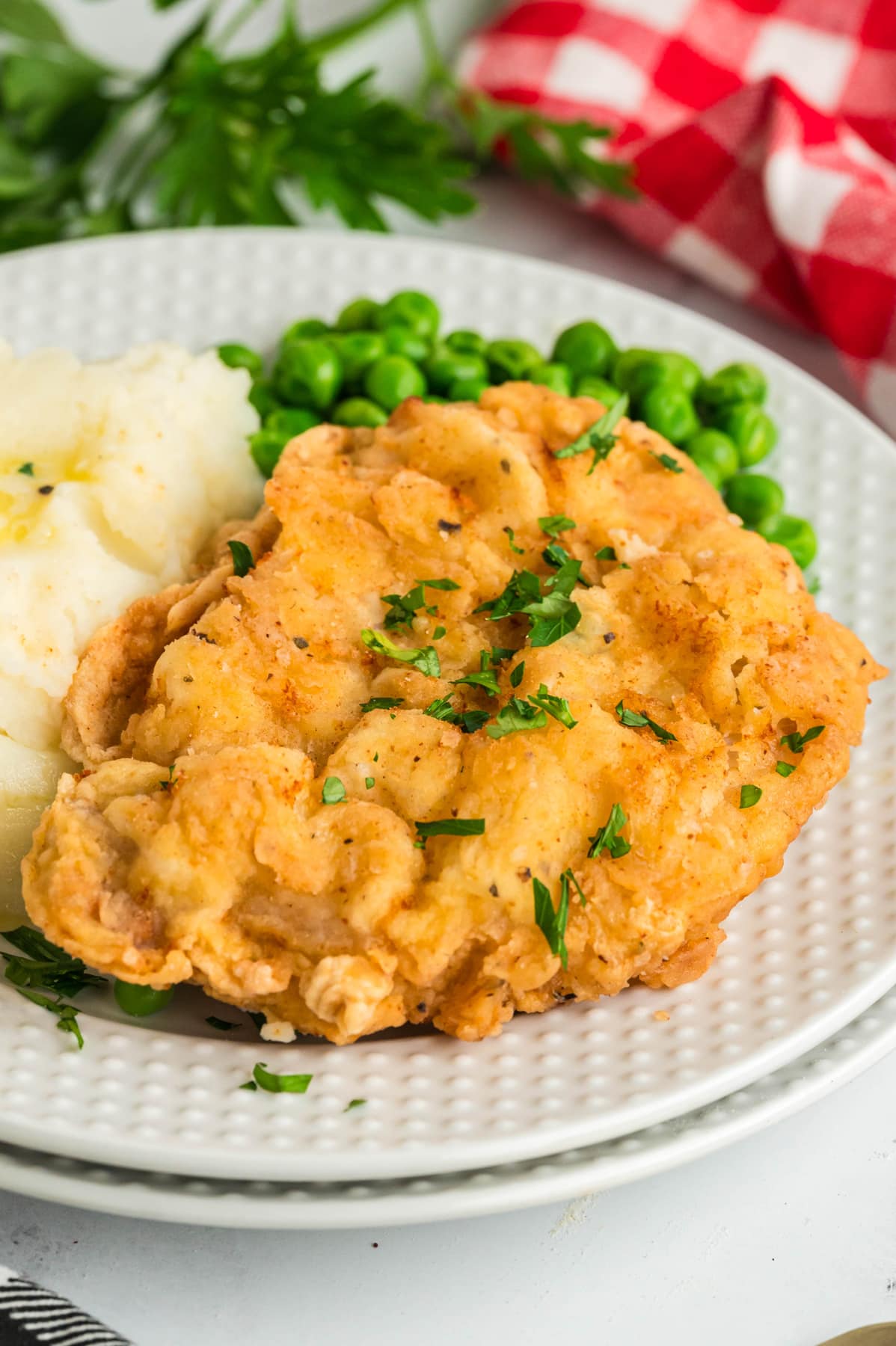 A breaded pork chop on a plate with mashed potatoes and peas