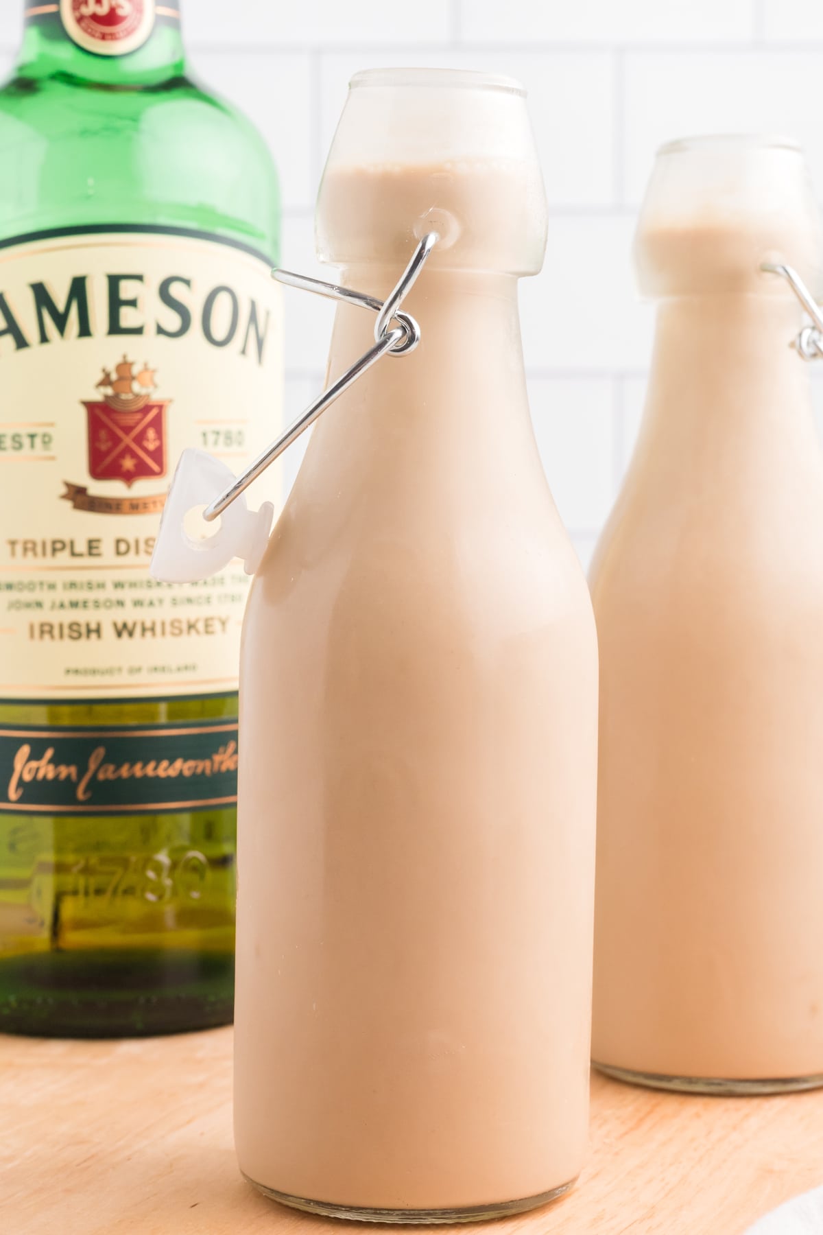 Two bottles of homemade Baileys in front of a bottle of Jameson