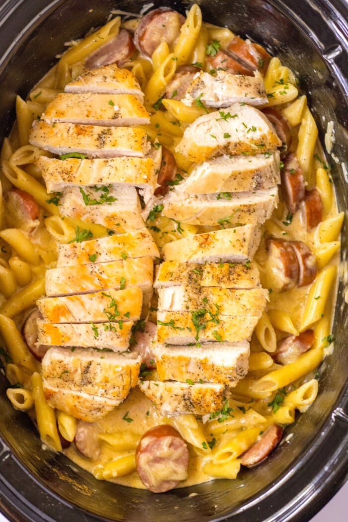 chicken sliced on top of sausage and pasta in slow cooker