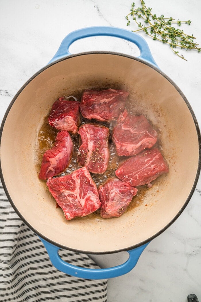 Pieces of chuck roast searing in a skillet