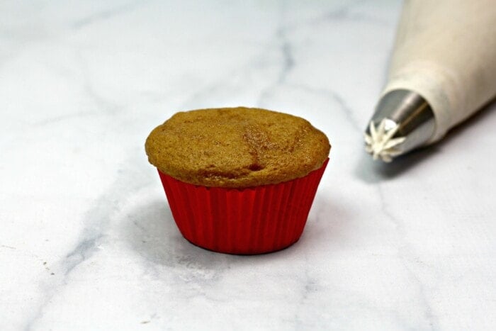 plain cupcake sitting with an piping bag
