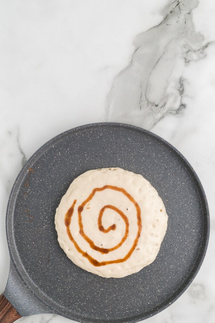 Pancake batter with a cinnamon swirl on a griddle