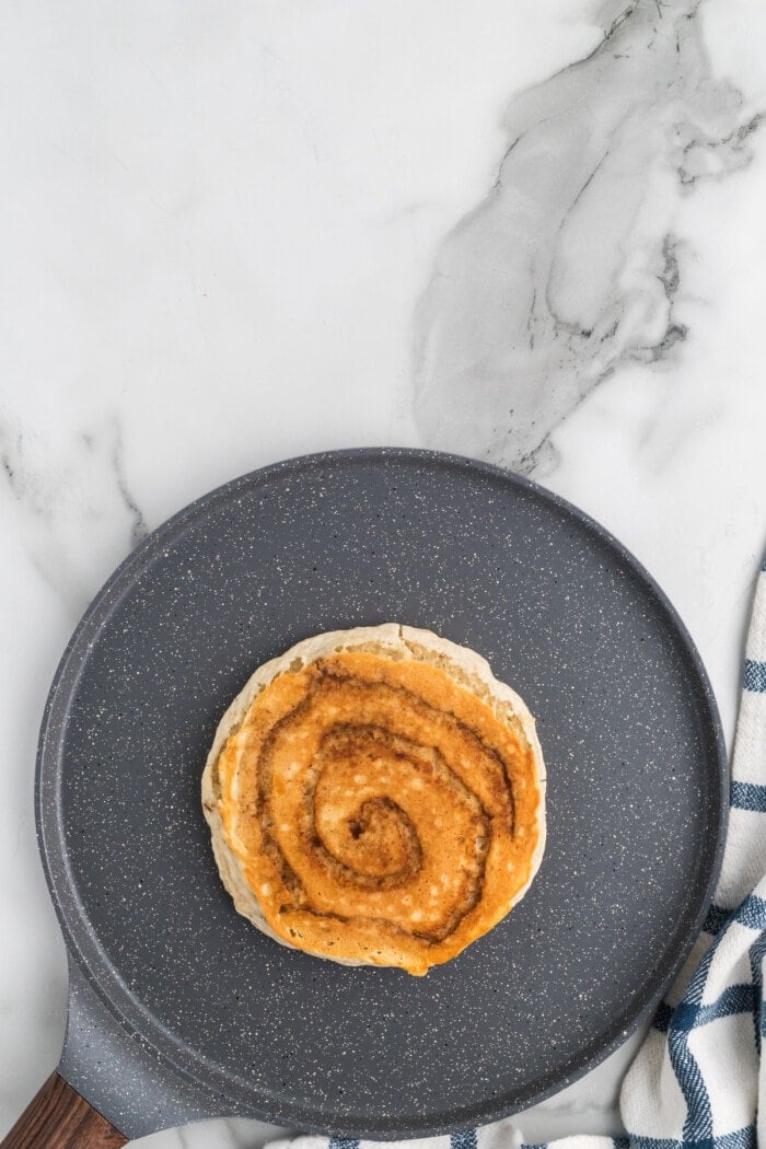 A cinnamon roll pancake on a griddle