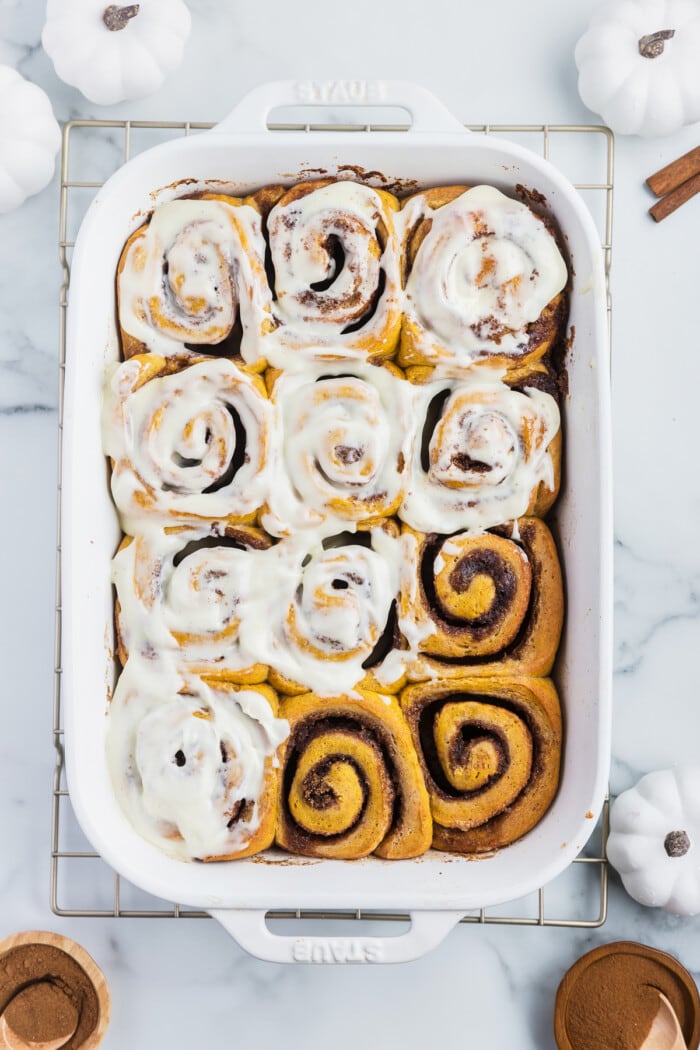 A baking dish of pumpkin cinnamon rolls, most covered with icing