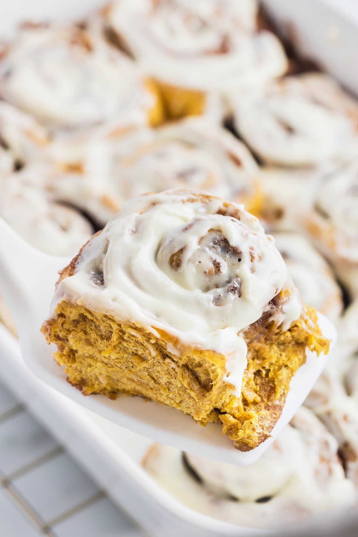 A pumpkin spice cinnamon roll lifted out of the pan