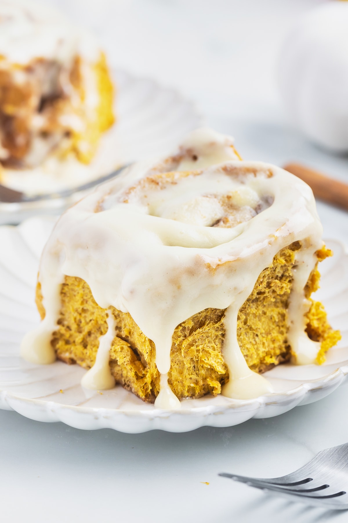 A pumpkin spice cinnamon roll with icing on a plate