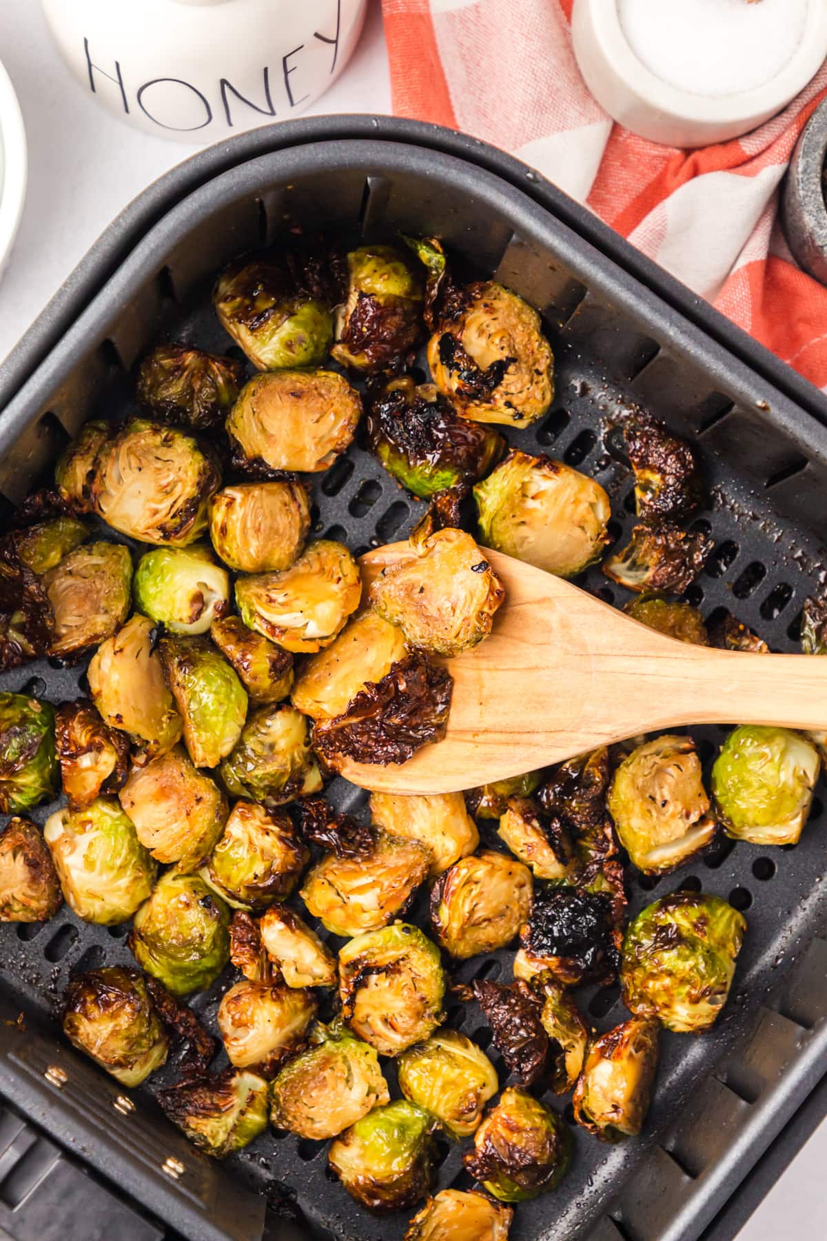 A wooden spoon stirring brussels sprouts in the air fryer