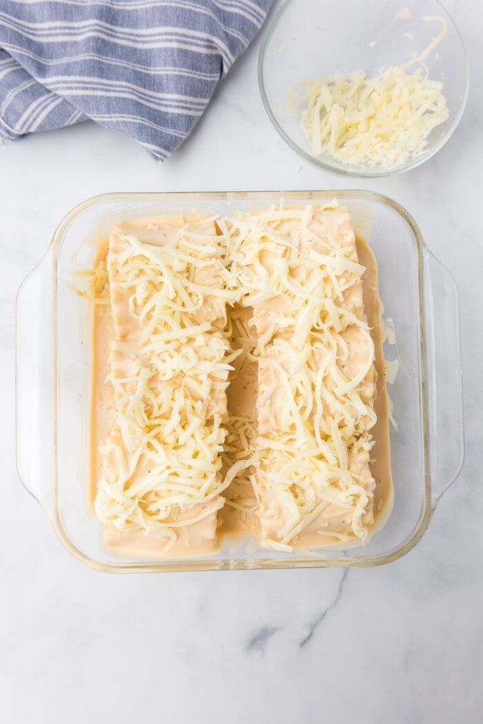shredded cheese on top of alfredo lasagna roll ups in baking dish