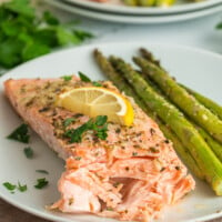 An oven baked salmon filet on a white plate with asparagus