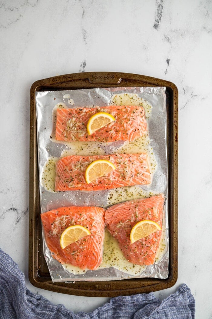 Four salmon filets on a baking sheet topped with lemon slices