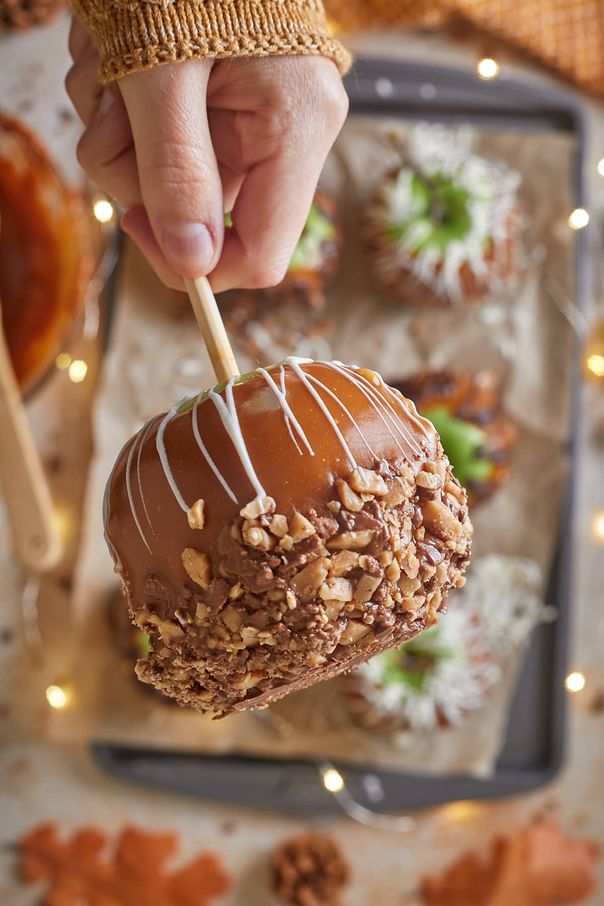 A hand holding a caramel apple dipped into toffee bits
