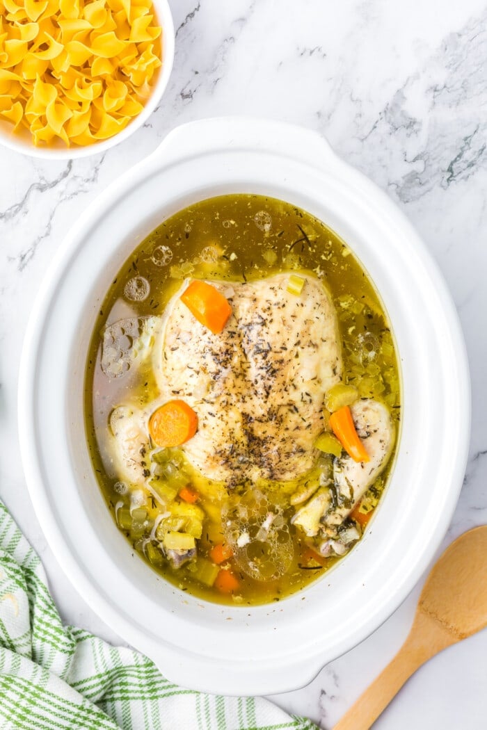 A whole chicken covered with broth in a crockpot