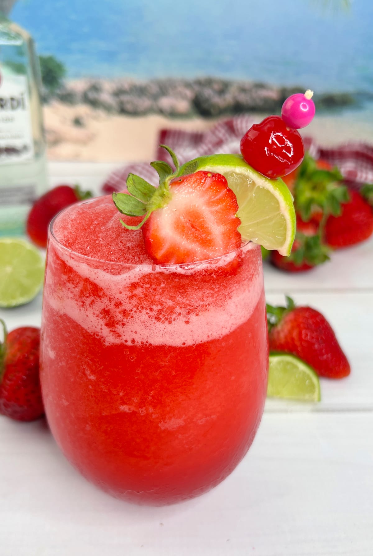 close up look at frozen strawberry daiquiri in glass with strawberry and lime garnish
