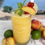 peach daiquiri in glass with fresh peach, cherry and lime on top