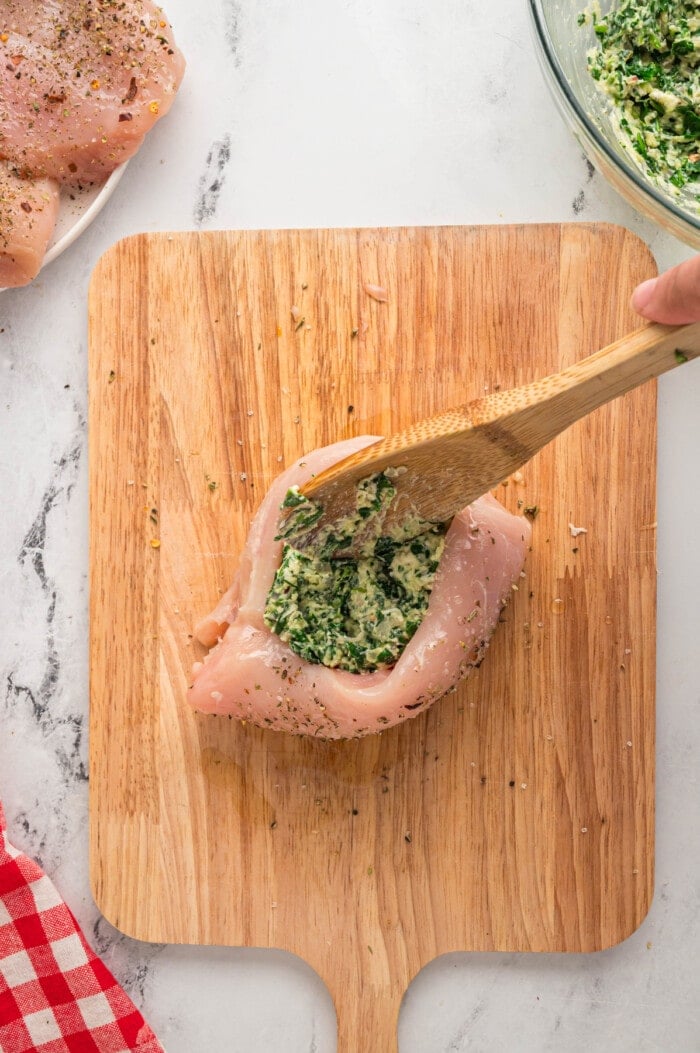 A wooden spoon stuffing a chicken breast with spinach