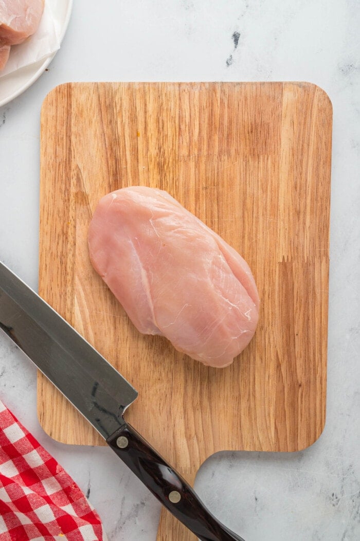 A raw chicken breast on a cutting board with a knife