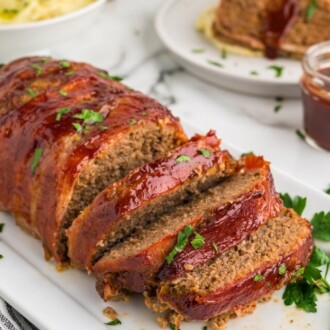 bacon wrapped meatloaf sliced on white serving platter