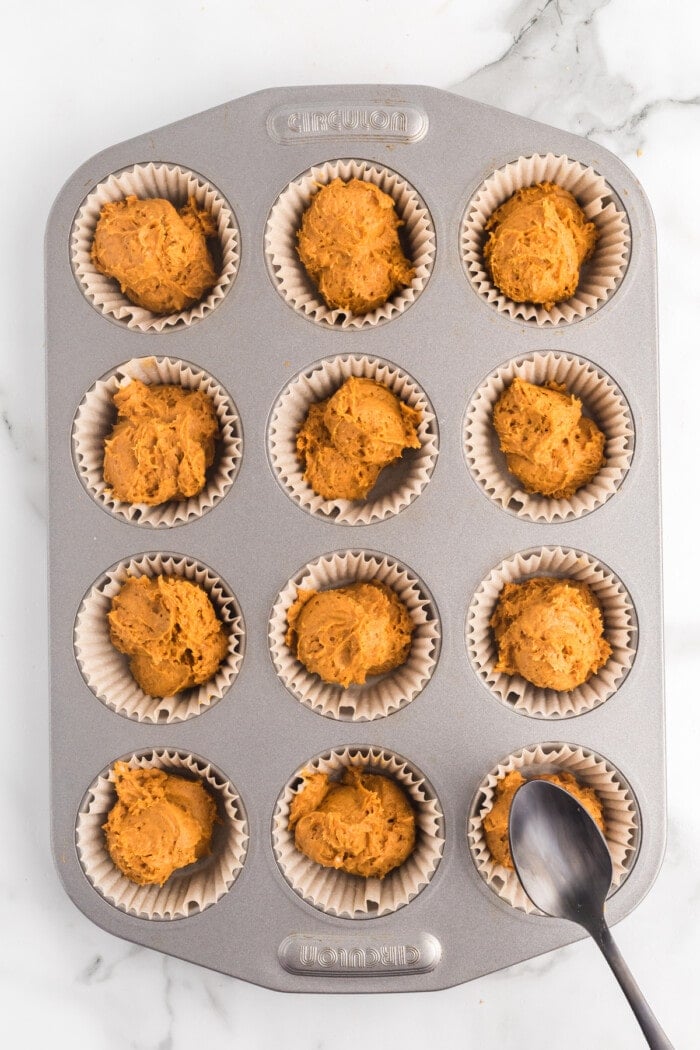 2 Ingredient Pumpkin Muffin batter in white cupcake liners in a baking sheet.