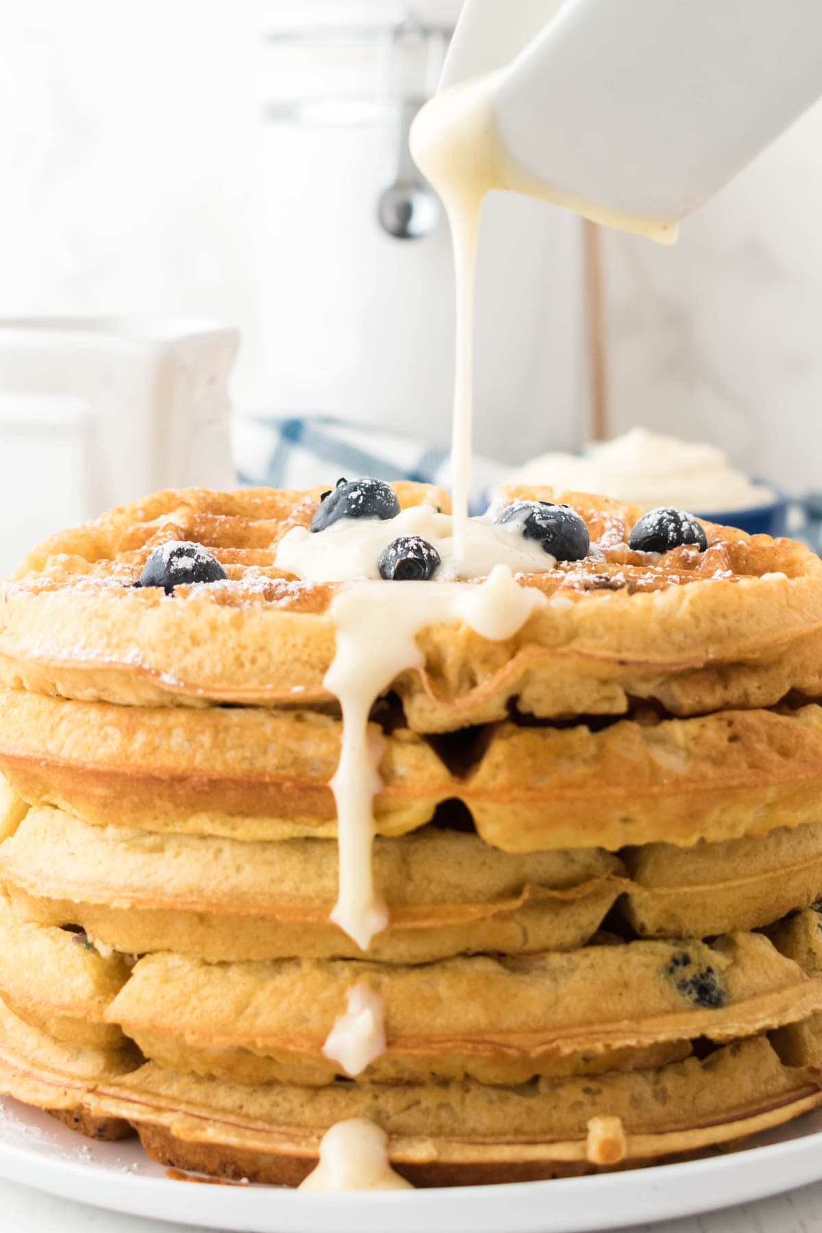 A stack of blueberry waffles being drizzled with cream.