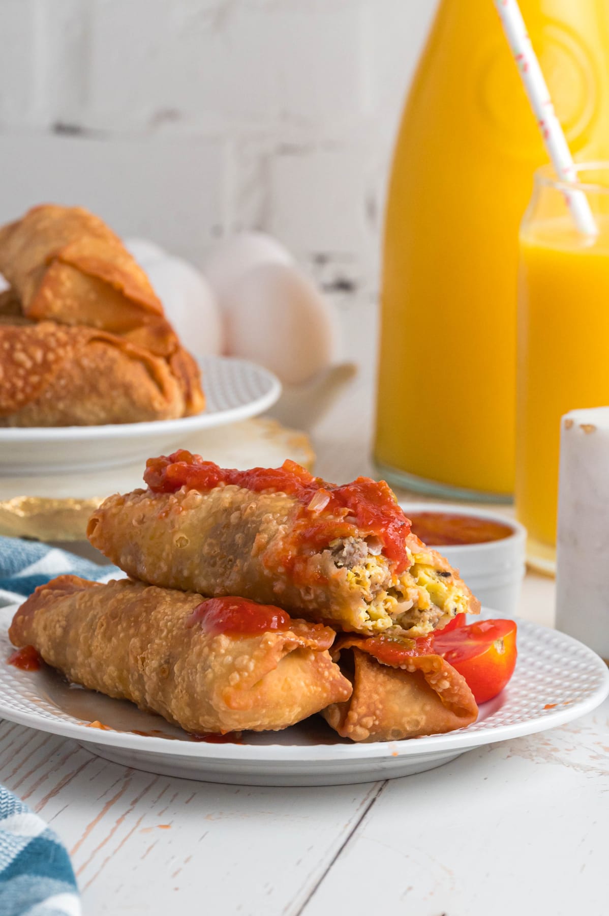 Breakfast egg rolls with salsa on a plate with orange juice.