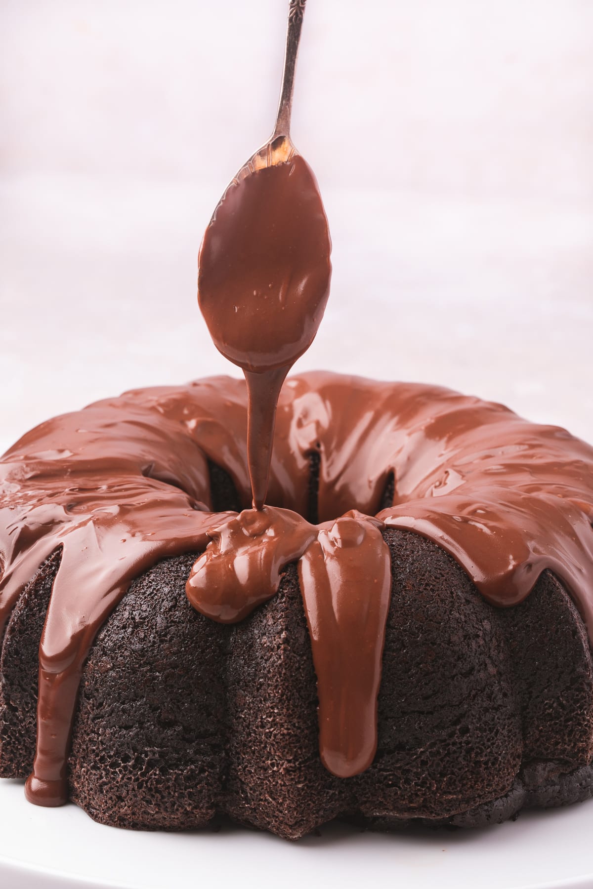 A spoon drizzling chocolate ganache over chocolate bundt cake