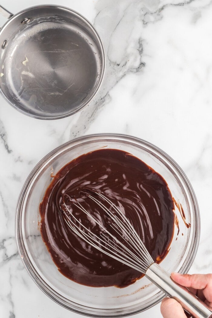 A whisk mixing chocolate ganache in a glass bowl