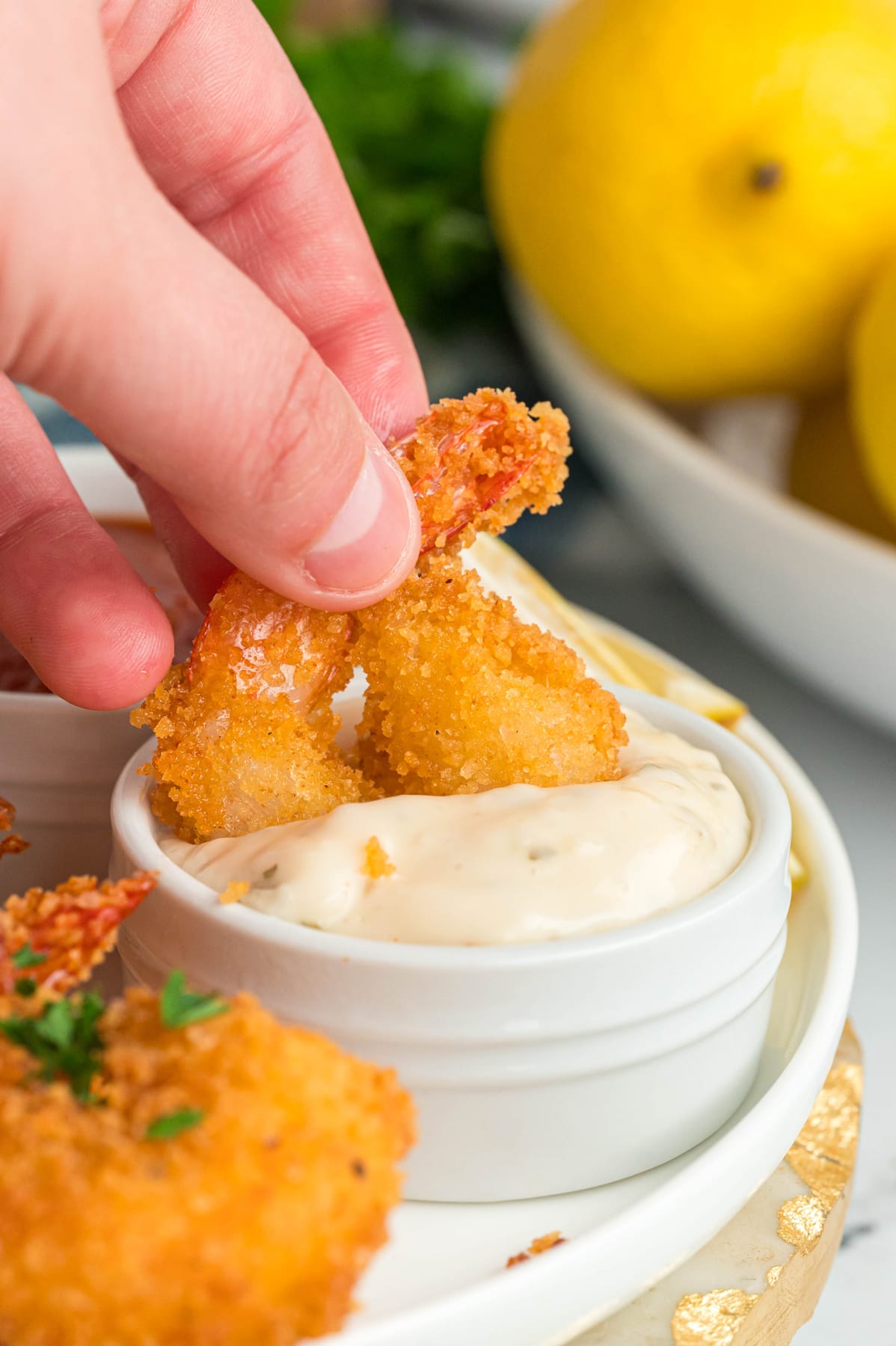 A hand dipping a fried shrimp into tartar sauce