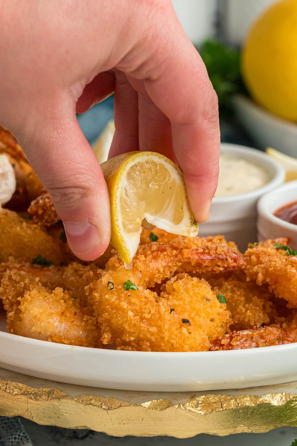 A hand squeezing a lime wedge over fried shrimp