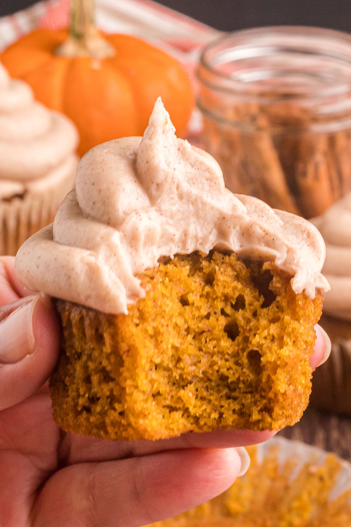 A hand holding a pumpkin cupcake with cream cheese frosting