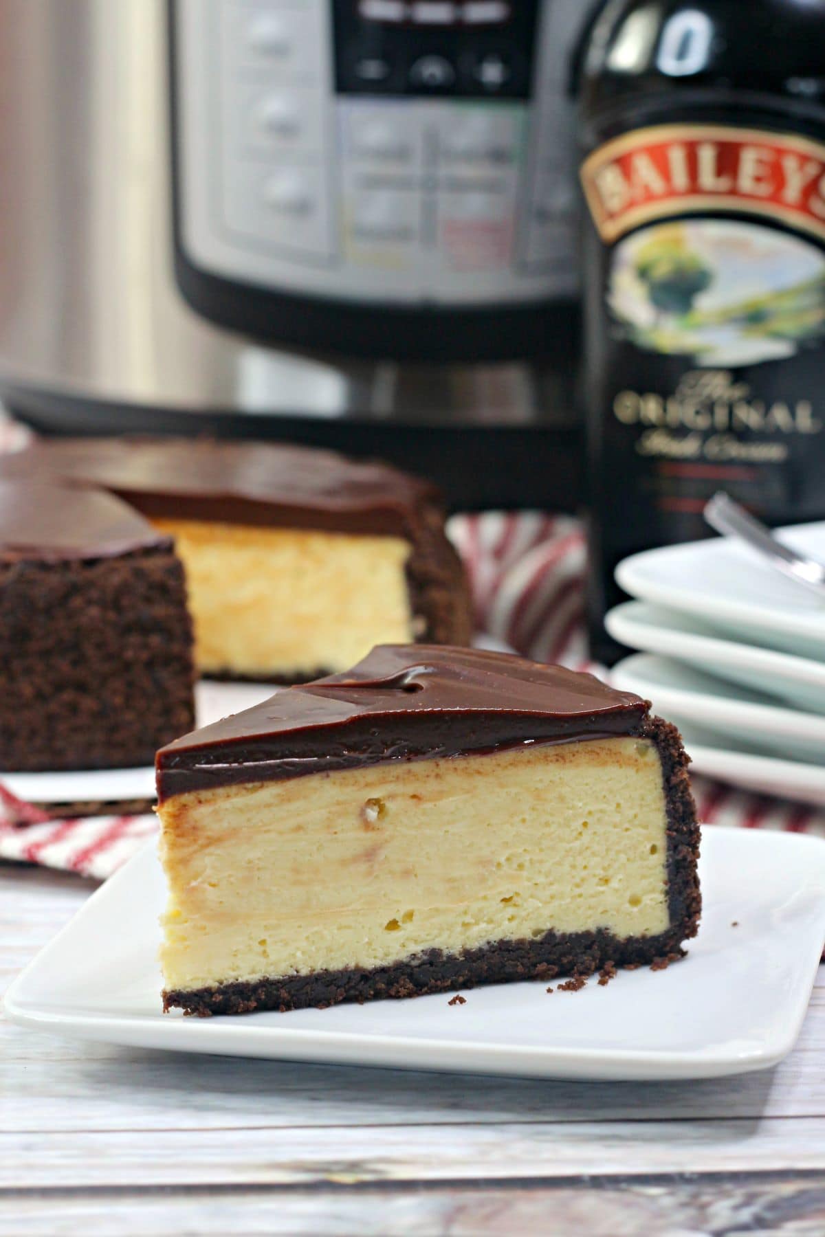 A slice of Baileys Cheesecake on plate with a bottle of Baileys and an instant pot in the background