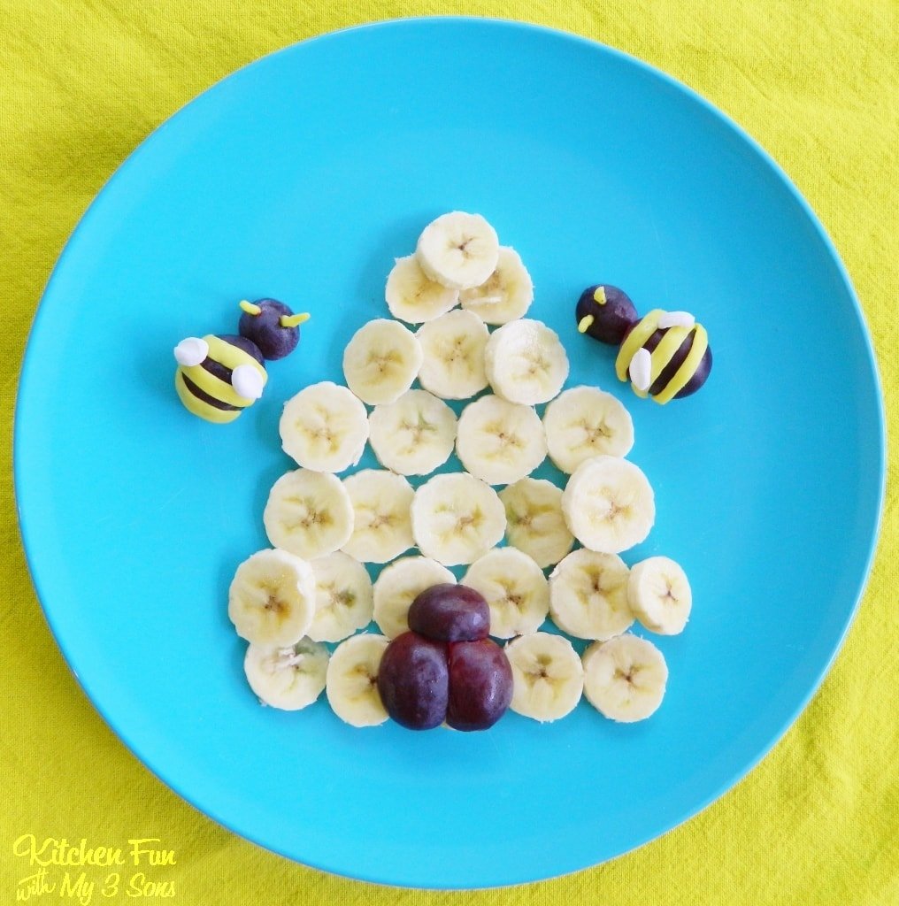 Bananas and grapes on a blue plate that resemble a bee hive and bees