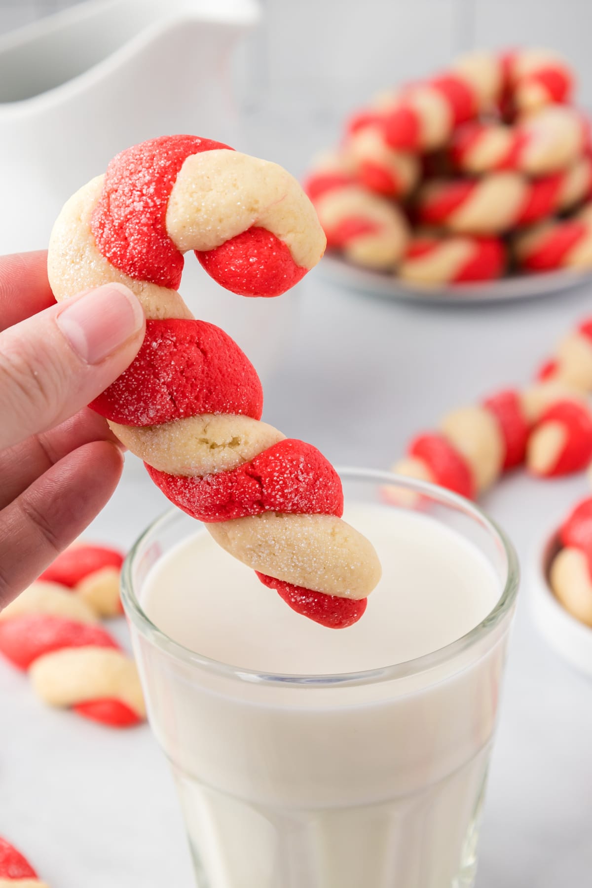 Candy Cande SHaped Cookies about to be dunked in a glass of milk.