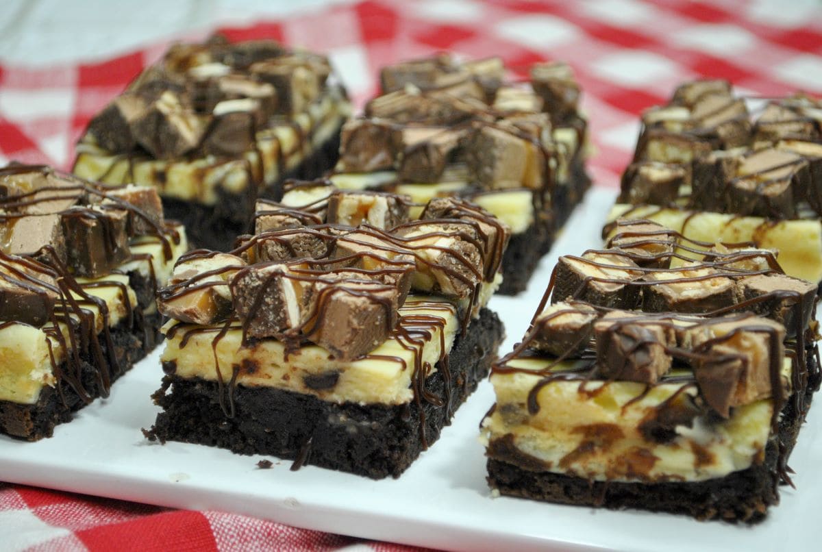 Several Snickers Cheesecake Brownies on a plate