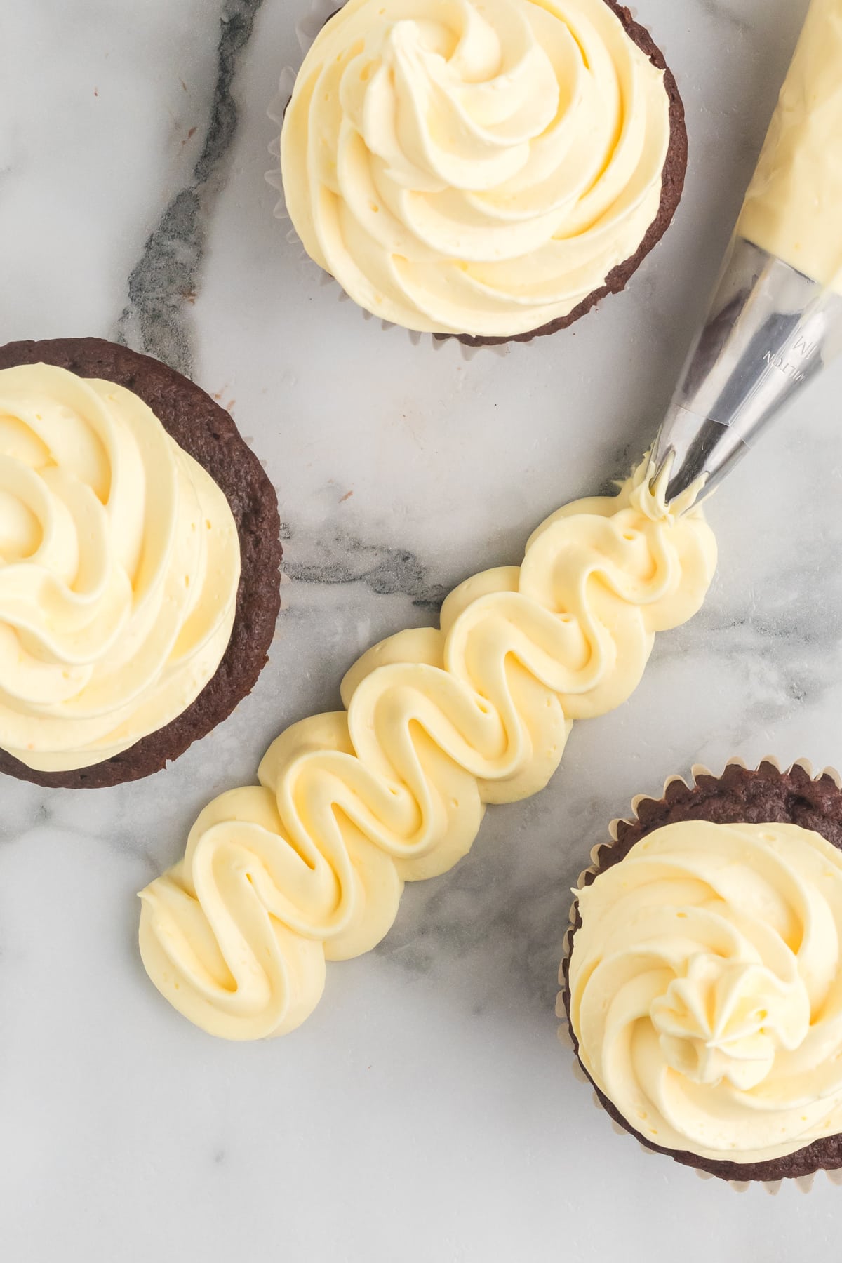 Cool Whip Frosting piped in a squiggly line on a marble countertop surrounded by cupcakes.