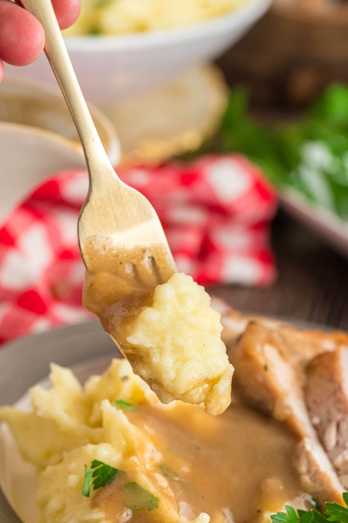 Mashed potatoes with gravy on a fork, held over a plate of potatoes