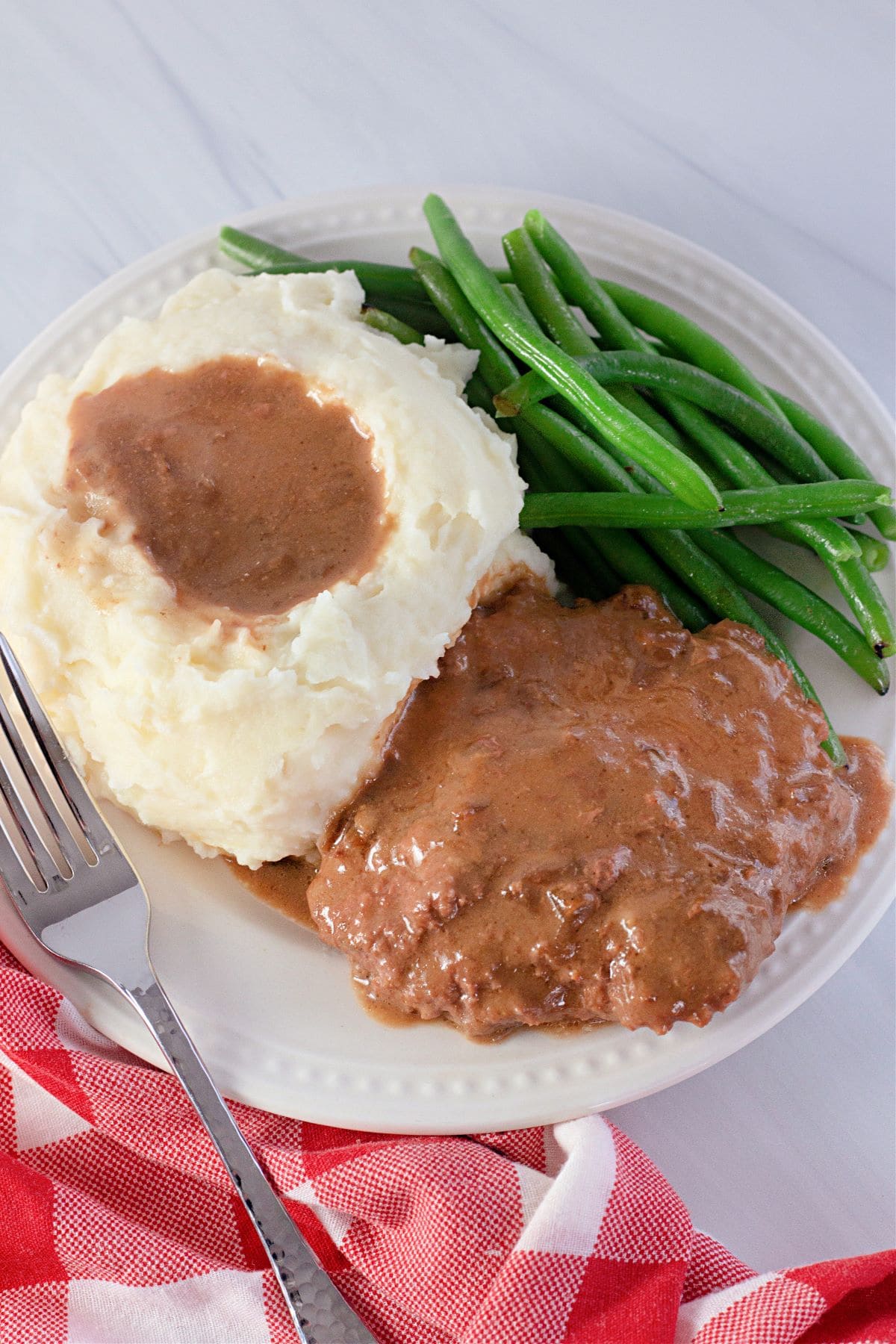 Crock Pot Cube Steak with Gravy on a plate with a fork with mashed potatoes and green beans