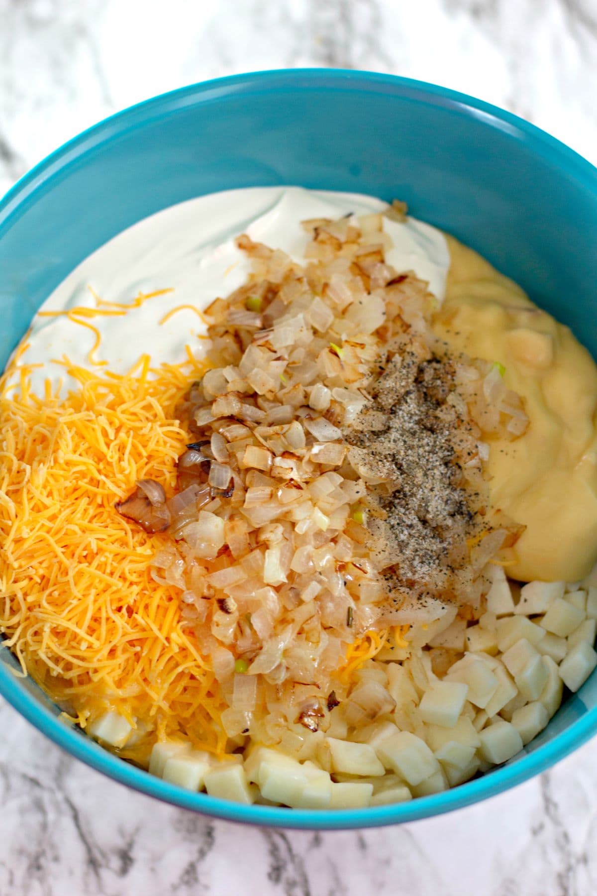 mixing together onions, cheese, sour cream, potatoes, butter, salt, pepper, and cream of chicken soup in a teal bowl
