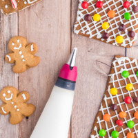 Icing in a piping bag alongside decorated gingerbread house pieces.