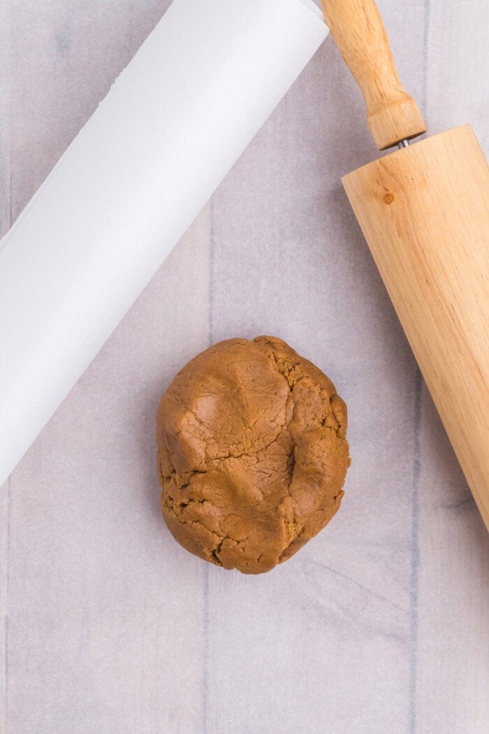 Gingerbread dough on parchment paper laying next to a wooden rolling pin.