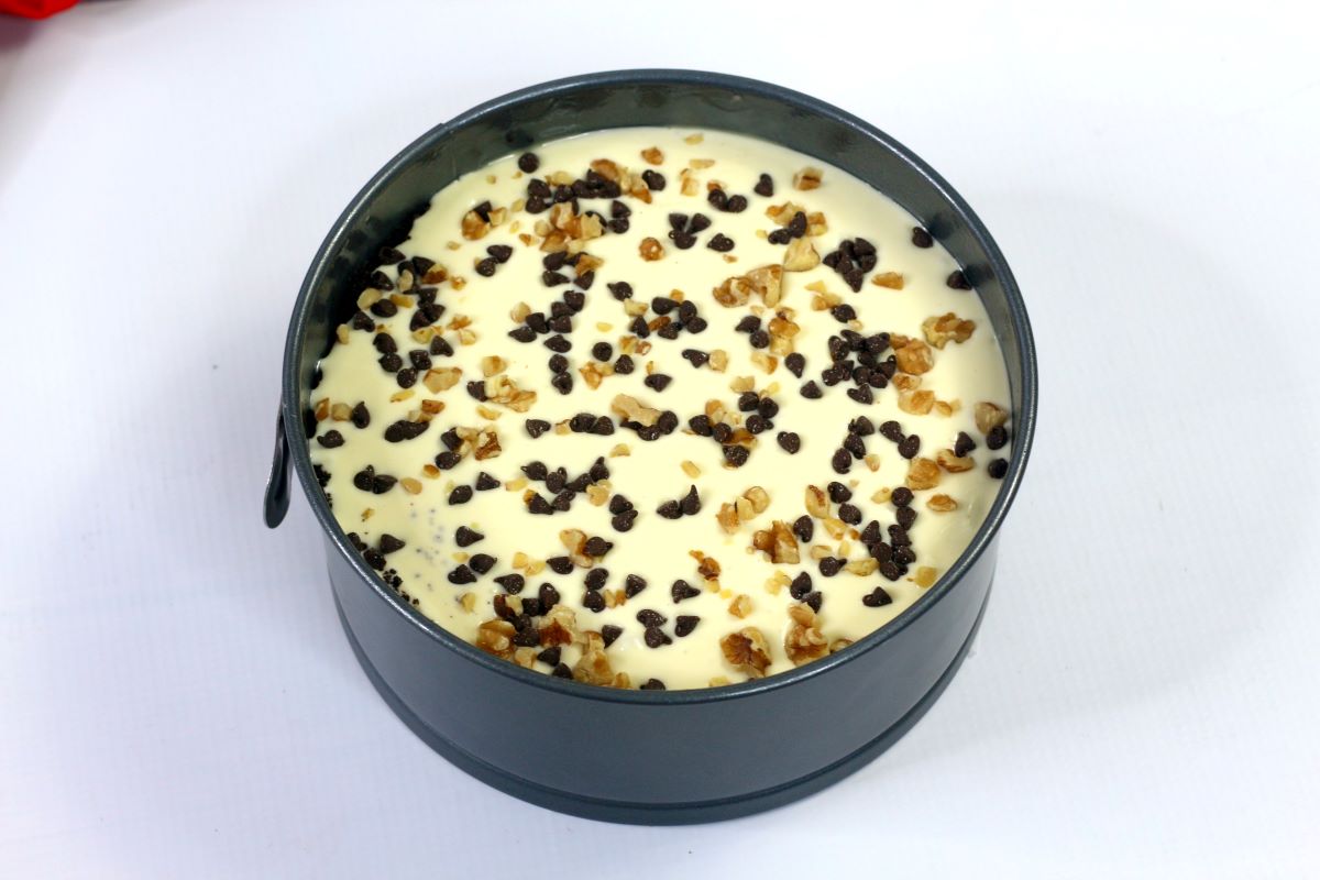 Cheesecake filling in a springform pan. with chocolate chips and walnuts on top.